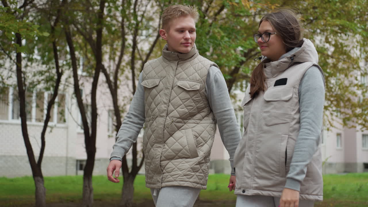 Wonderful moment of couples walking outdoors in matching outfits, swinging hands while warmly looking at each other with affection, surrounded by trees and soft urban background