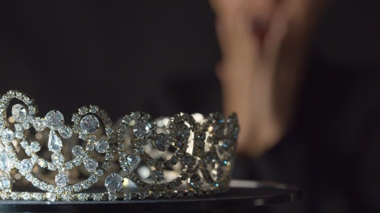Una reginetta di bellezza o una sposa, pensierosa e con lo sguardo sfocato, alza gli occhi e vede la corona dei suoi sogni, rimanendo sorpresa e poi tentata di prenderla.