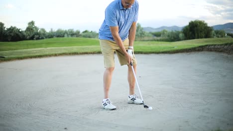 a male golfer preparing to hit his ball out of the sand trap onto the green