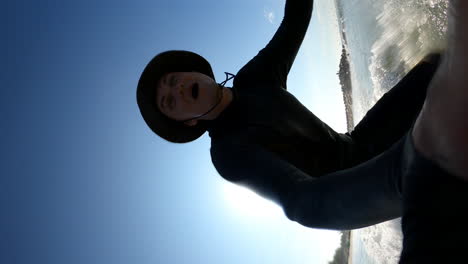 Vertical-Shot-Of-A-Male-Surfer-Taking-Selfie-With-Handheld-Action-Camera-While-Surfing-In-The-Sea-In-Summer