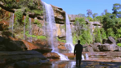 Junger-Mann,-Der-Den-Unberührten-Natürlichen-Wasserfall-Genießt,-Der-Tagsüber-Von-Der-Bergspitze-Fällt,-Aus-Einem-Niedrigen-Winkelvideo,-Das-Bei-Phe-Phe-Fall-Meghalaya-Indien-Aufgenommen-Wurde