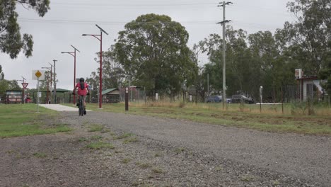 Solo-Ciclista-De-Montaña-Cabalgando-Hacia-Un-Pequeño-Pueblo-Rural-En-Queensland,-Viajando-A-Lo-Largo-De-Un-Camino-De-Grava