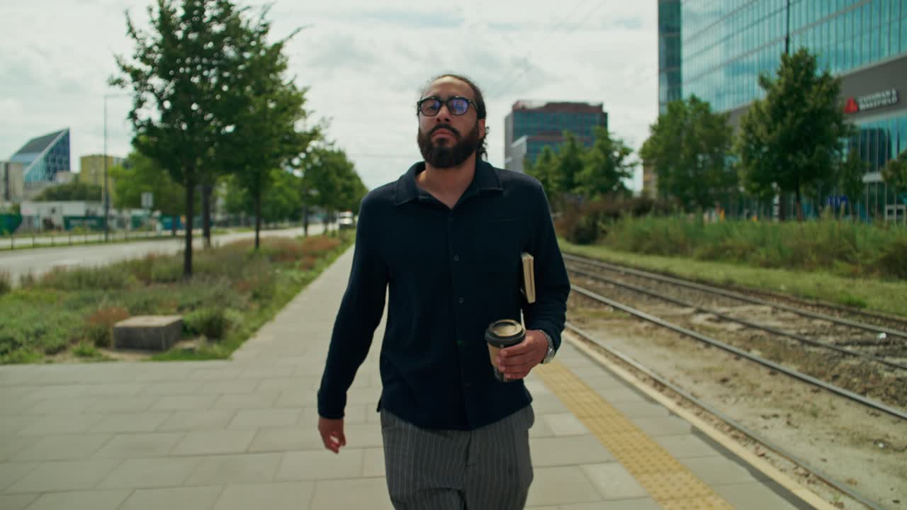 Uomo che cammina sul marciapiede con un caffè in un ambiente urbano
