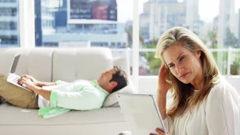 young woman digital tablet while man using laptop in background at home