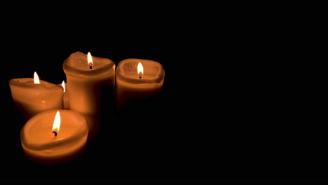 grupo de cuatro velas encendidas sobre fondo negro, fuego naranja y velas