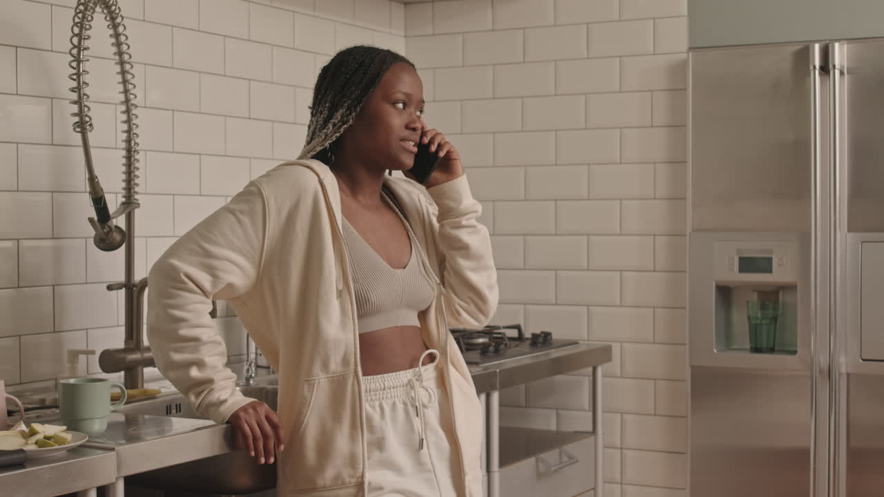 Young Black Woman Chatting on Phone in Kitchen