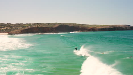 Aerial:-Surfing-the-beach-of-Bordeira-in-the-Algarve,-Portugal