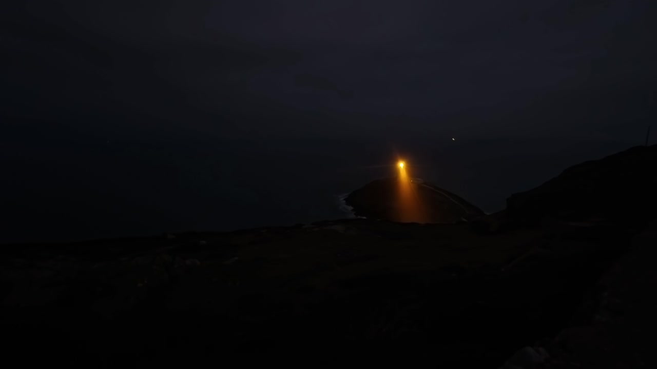 Bright lighthouse lamp illuminating coastal island time lapse on a dark early morning