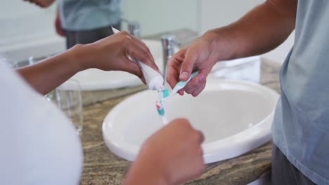 Sección-Intermedia-De-Una-Pareja-De-Raza-Mixta-Poniendo-Pasta-De-Dientes-En-El-Cepillo-Del-Baño