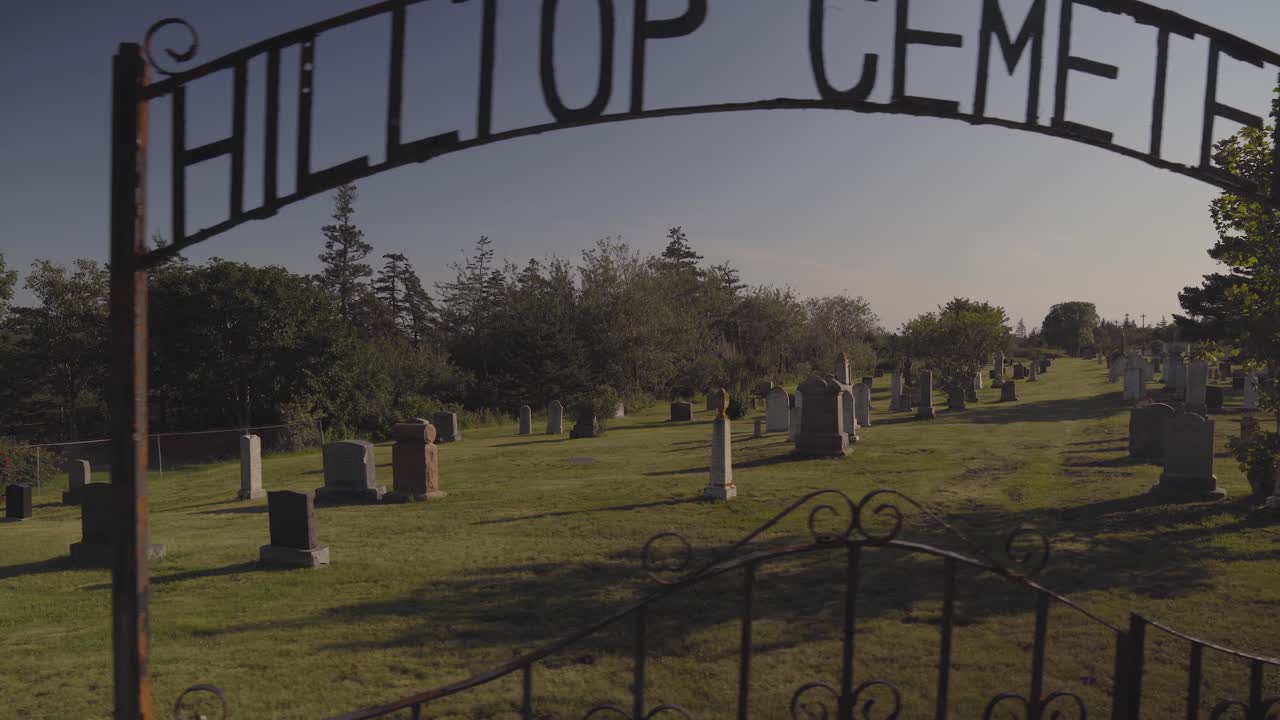 The Hilltop Cemetery. An old cemetery on Brier Island Nova Scotia on a sunny day in the late afternoon. A walking pan across the gate and down with headstones in the background