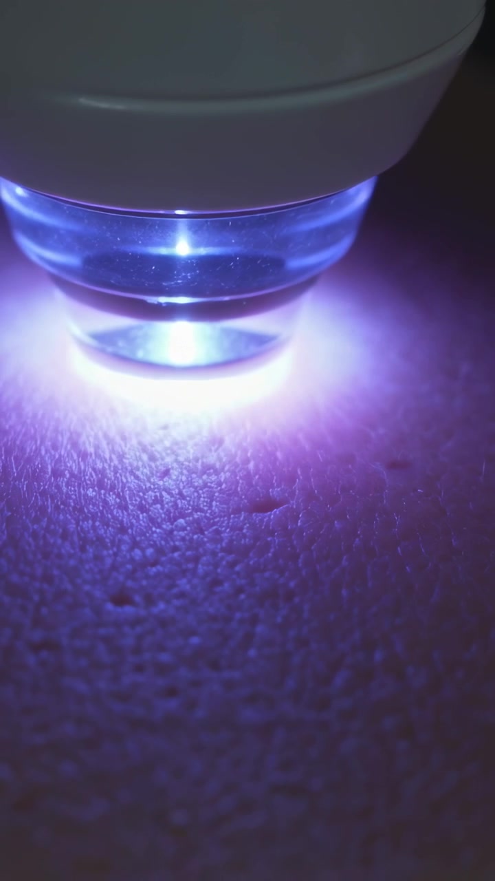 Video vertical: Punta de succión en contacto, dispositivo activando LED violeta sobre piel desnuda, tratando una imperfección