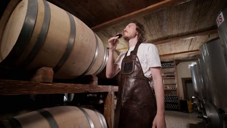 authentic shot of successful male sommelier is tasting a flavor and checking white wine quality poured in transparent glass in a wine cellar.