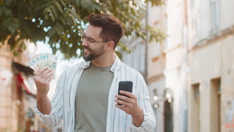 happy caucasian man counting money euro cash using smartphone calculator app on city street