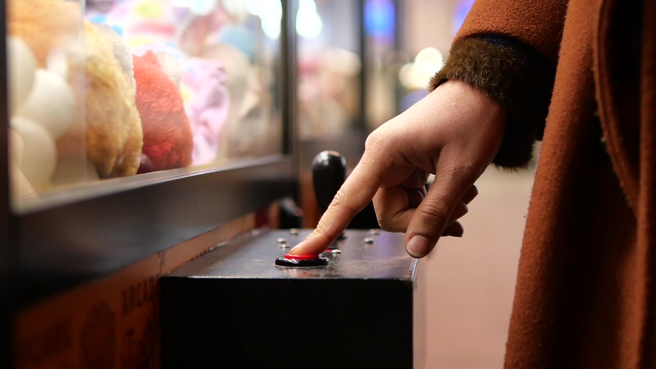 Close-up of a Hand Pressing a Red Button on an Arcade Claw Machine