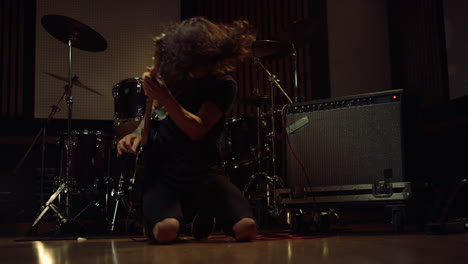 Expressive-guitarist-playing-electric-guitar-on-knees-in-recording-studio