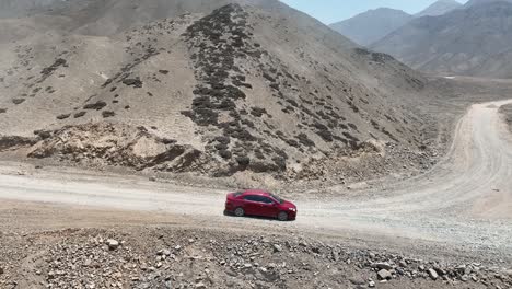 toma panorámica aérea de un viaje por carretera con un camión rojo en un camino seco y polvoriento con piedras a lo largo de las colinas hasta la ciudad santa de caral en perú en un día soleado