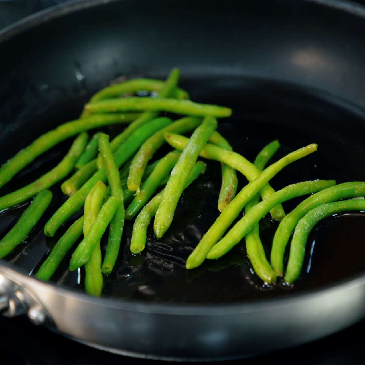 Unrecognized chef's hand in black glove puts the green beans on the frying pan. Cooking veggies close up. Vertical view