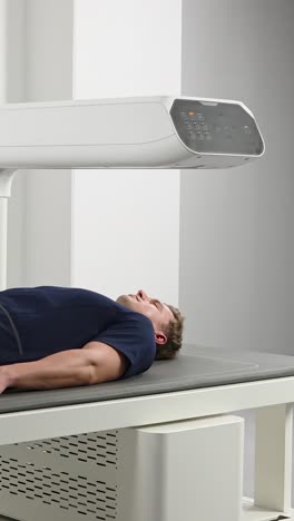 a caucasian man in his 30s lies still on a table while a modern medical scanner (dexa) moves over his body to analyze bone density and body composition in a clinic.