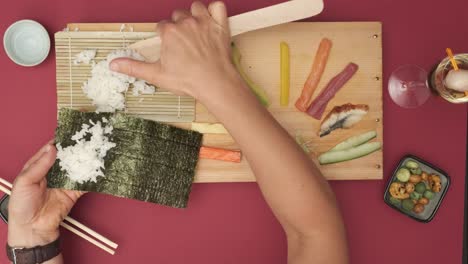 Top-shot-of-two-Hands-preparing-Sushi-on-red-table