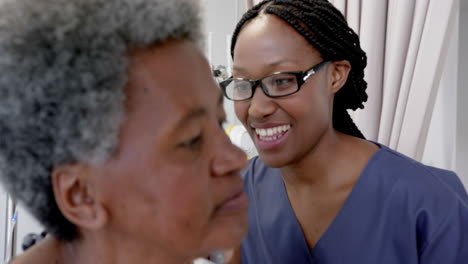 African-american-female-doctor-testing-ear-of-senior-female-patient-in-hospital-room,-slow-motion