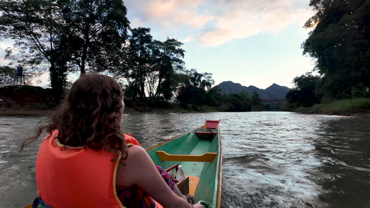 Donna che viaggia in barca a coda lunga lungo il fiume Nam Song al tramonto, con indosso un giubbotto di salvataggio