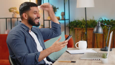 Happy-amazed-Indian-man-guy-working-on-smartphone-celebrate-victory-winning-lottery-at-home-office