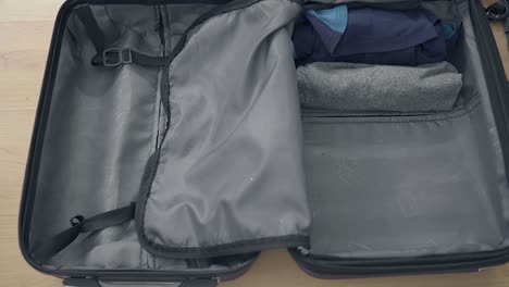 close up shot of male person packing small suitcase, carefully put dresses into