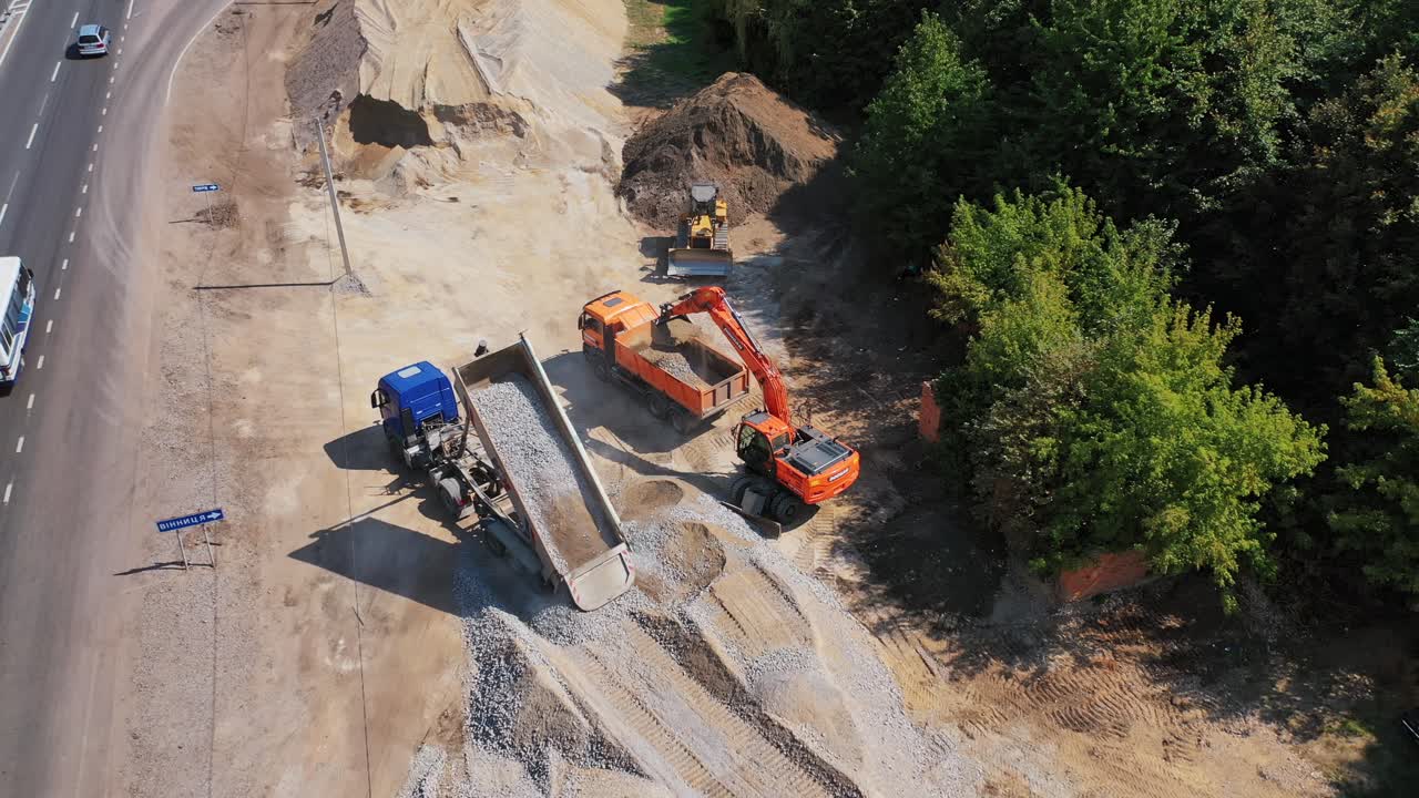 Excavator loads rubble into a truck. Large truck scattering small broken stone on the pile. Heavy machinery working outdoors in summer. Aerial view.