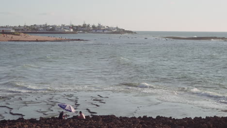 dos amigos bajo un paraguas, disfrutando de las vistas de la ciudad, con las olas del océano atlántico frente a ellos