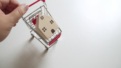 an individual pushing close-up of a tiny cart with a small wooden toy house in it