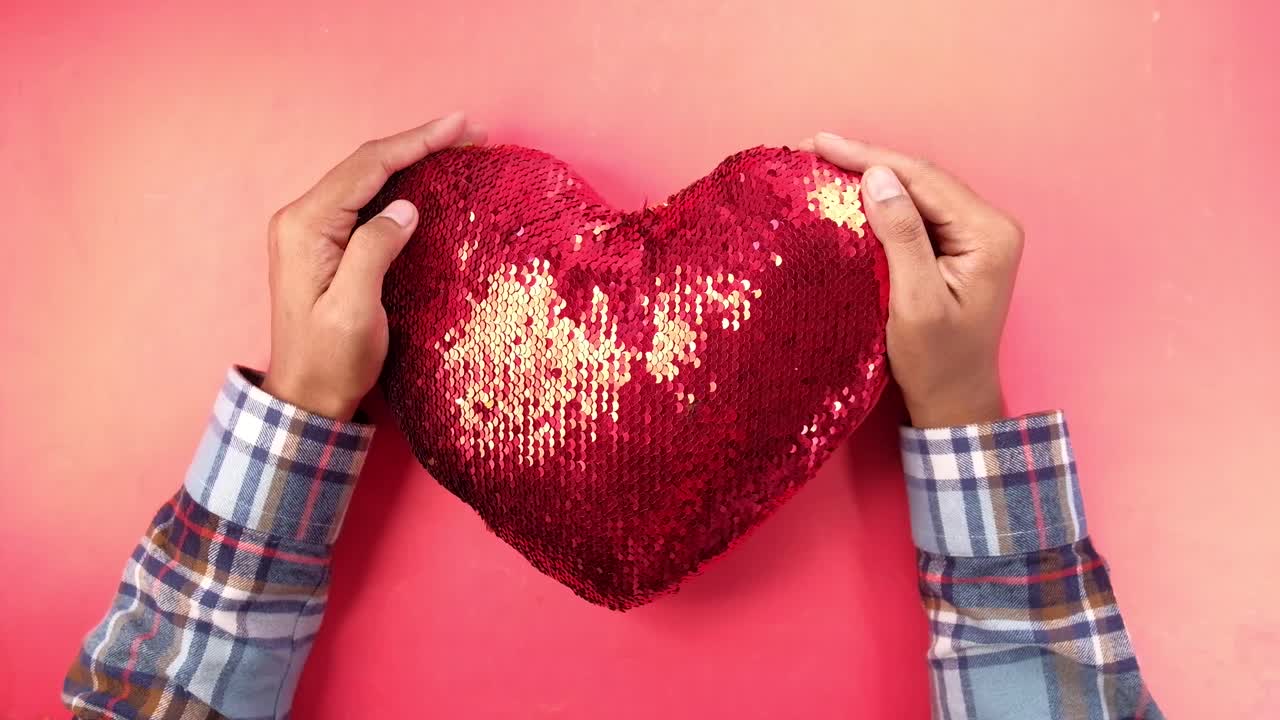 손은 빨간색 세킨 심장 모양의 베개를 들고 있습니다.