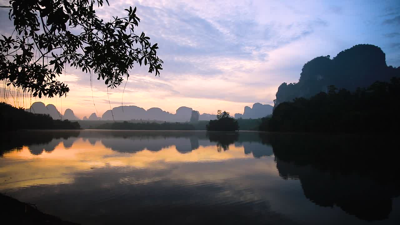 Scenic landscape sunset over a lake in Krabi, Thailand with a silhouette of trees and mountains in the background
