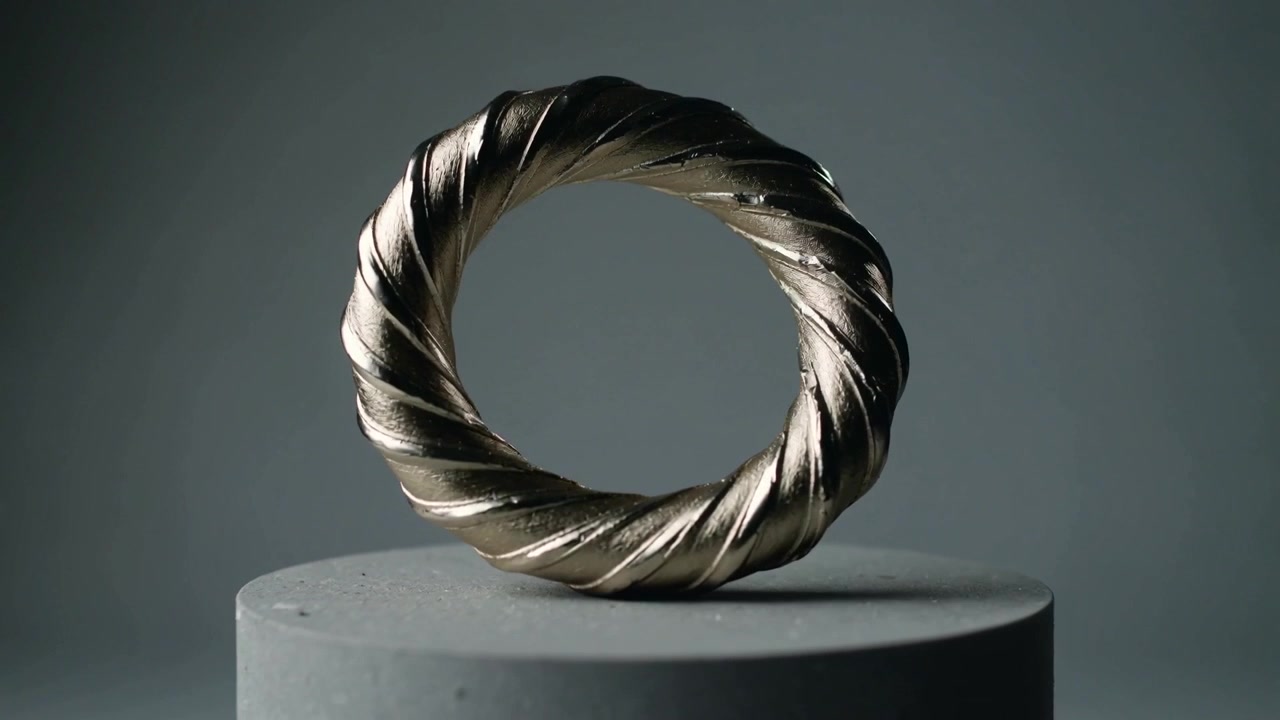 Spinning by motor, twisted torus ring settling upright on studio plinth, revealing bimetal braid