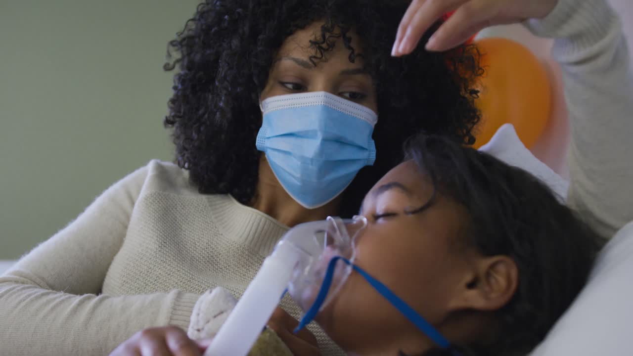 아프리카계 미국인 어머니 가 병원 침대에 누워 산소 마스크를 쓰고 딸을 돌보고 있습니다.