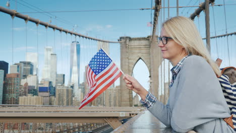 Eine-Frau-Mit-Der-Flagge-Von-Amerika-In-Der-Hand-Steht-Auf-Der-Brooklyn-Bridge-Mit-Blick-Auf-Manhattan