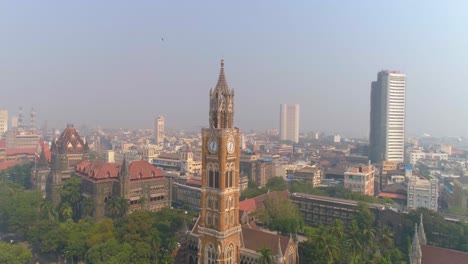 Drone-shot-of-the-Rajabai-Clock-Tower-next-to-the-Bombay-High-Court-Building-and-Oval-Maidan,-an-ornate-1878-clock-tower-modeled-after-Big-Ben-and-featuring-stained-glass-windows-and-musical-chimes