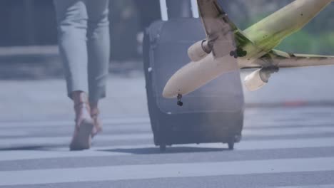 airplane flying against low section of woman with trolley bag crossing the street