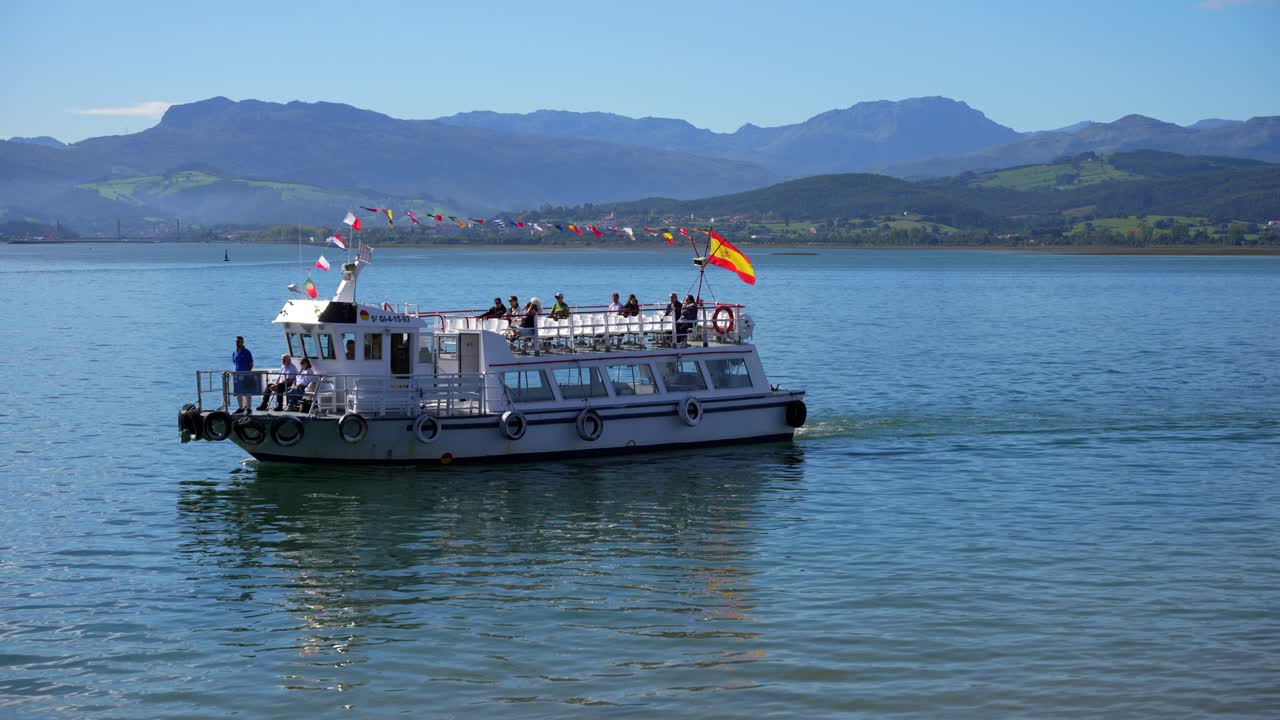 Tourist boat with Spanish flag cruises on the calm Cantabrian Sea near Santona and Laredo in background