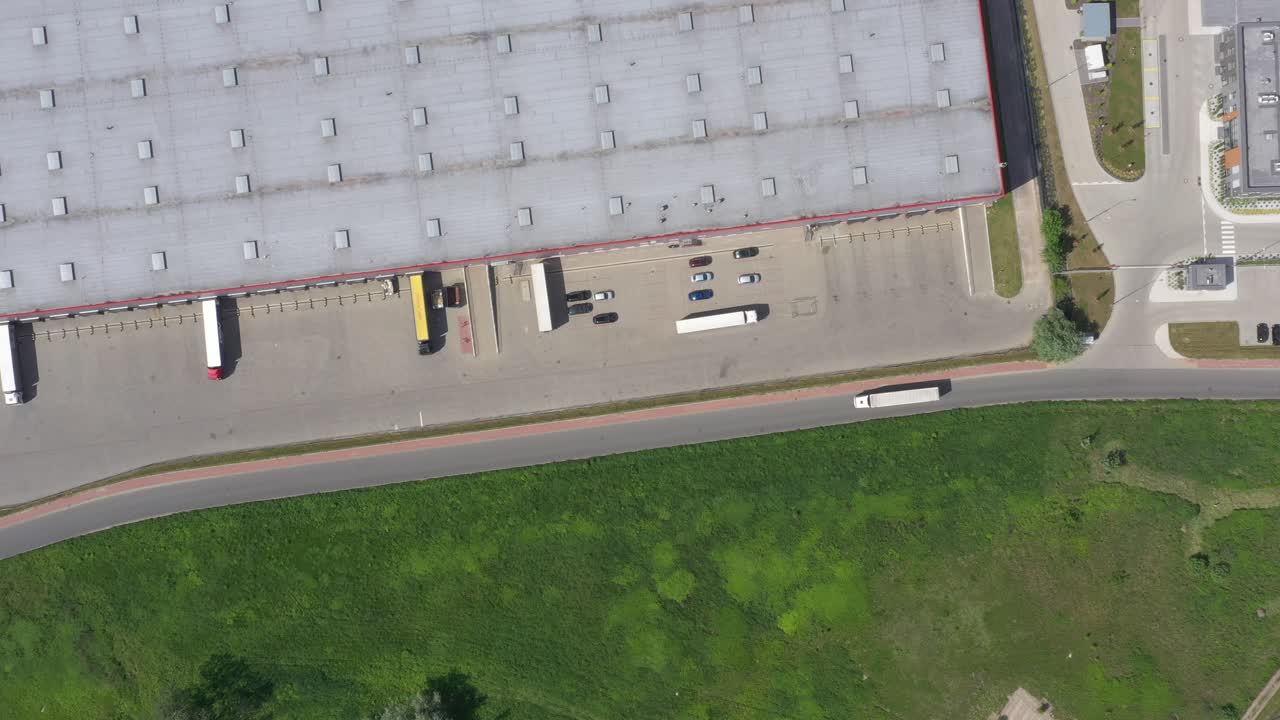 toma aérea de un camión con un semirremolque adjunto que sale del almacén industrial- edificio de almacenamiento- área de carga donde muchos camiones están cargando- descargando mercancías