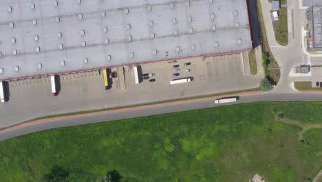 aerial shot of truck with attached semi trailer leaving industrial warehouse- storage building- loading area where many trucks are loading- unloading merchandise