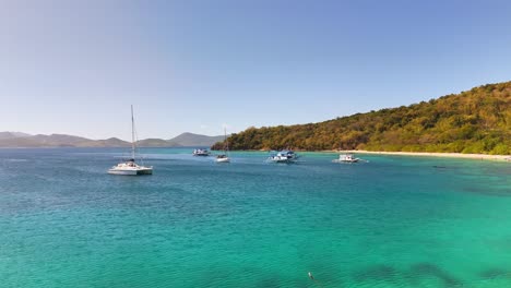 turquoise waters surround ditaytayan island in the philippines, where several boats are anchored near a lush, forested shoreline under a clear blue sky