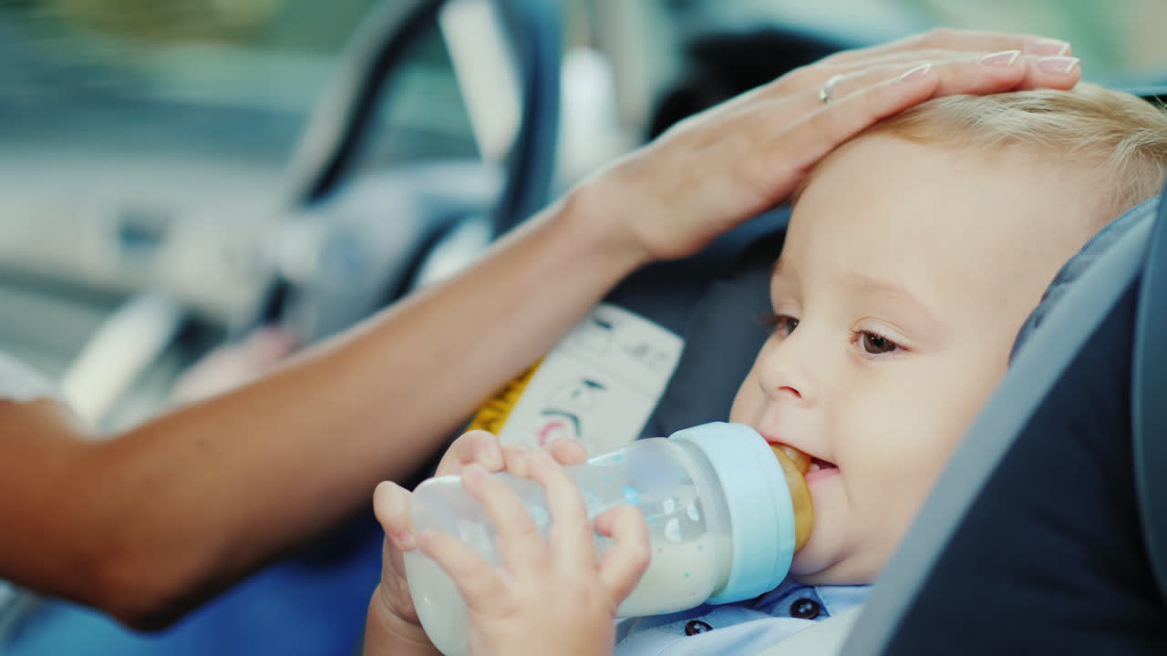 bebé de 1 año bebe leche de una botella se sienta en un asiento de coche para niños video 4k