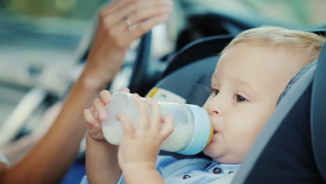 bebé de 1 año bebe leche de una botella se sienta en un asiento de coche para niños video 4k