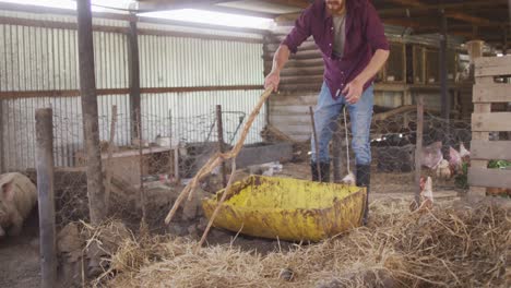 hombre caucásico trabajando en una granja, limpiando una pocilga