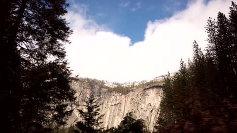 a break in the dense pine forests of yosemite national park reveals a bright, granite, tree lined, snow covered mountain in the distance