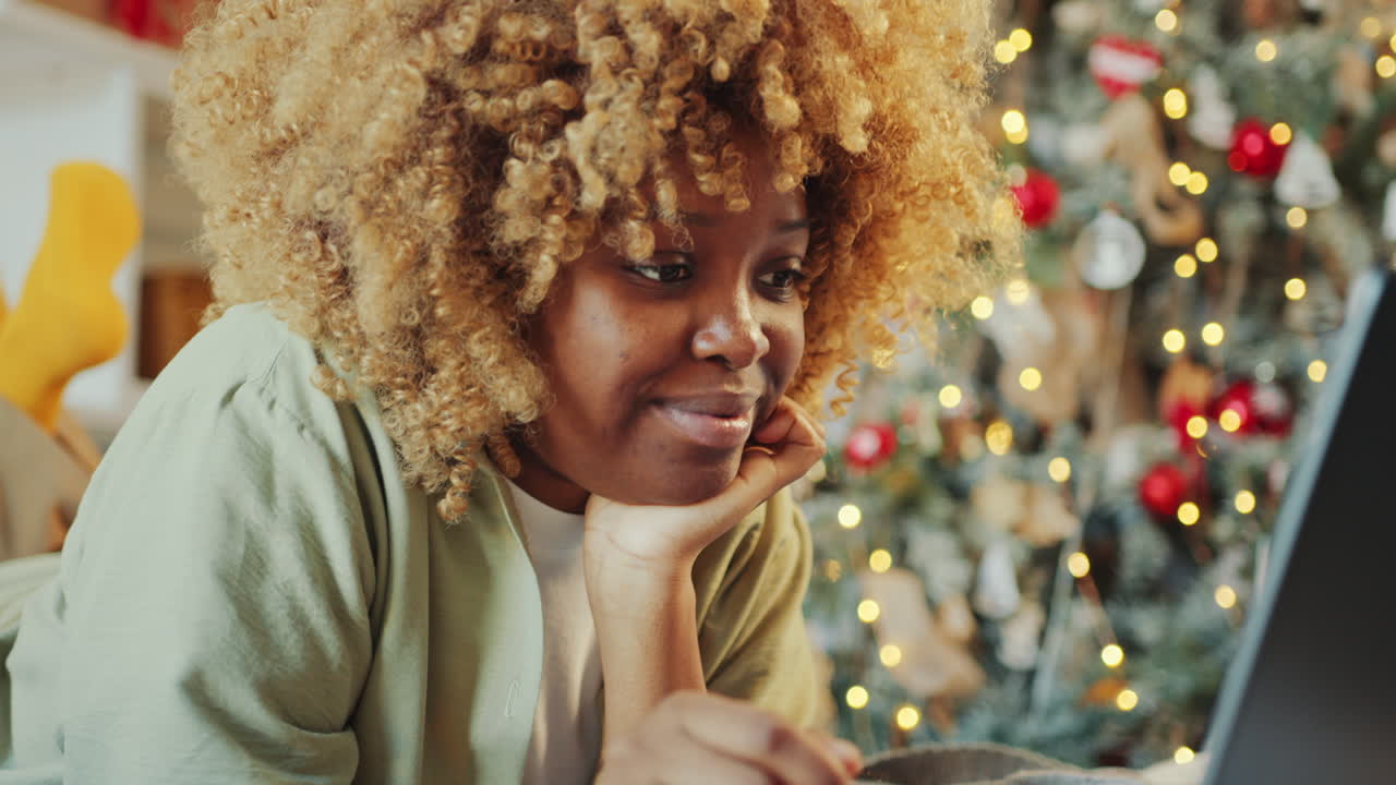 Woman Resting on Bed and Using Laptop in Room Decorated with Christmas Tree