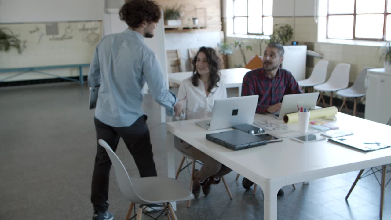 Back view of curly man walking to cheerful colleagues
