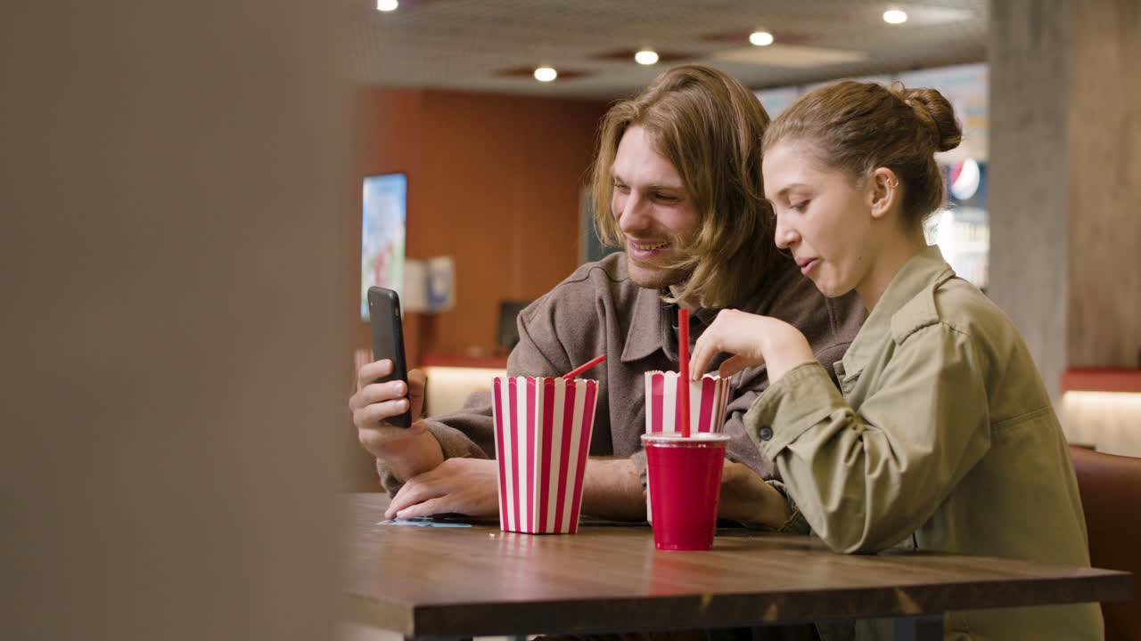pareja feliz tomando selfie con smartphone mientras come palomitas de maíz en el snack bar del cine 1