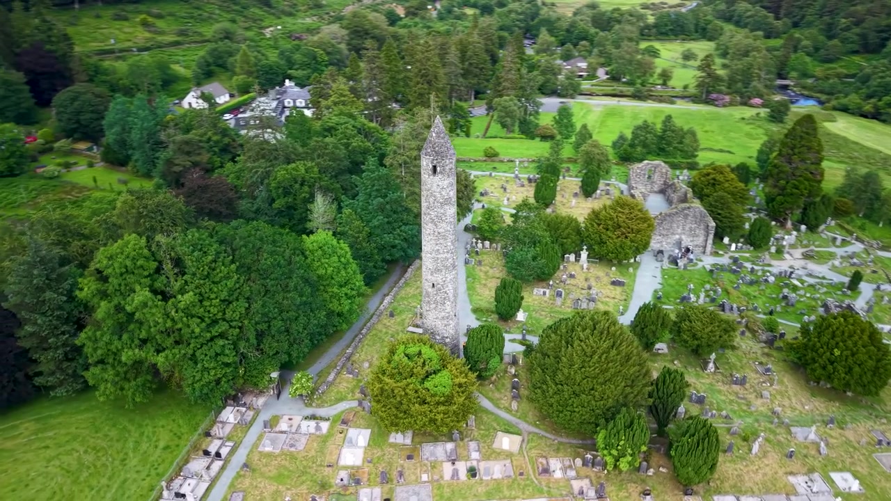 Panoramica con drone di un'iconica torre a Glendalough con cimitero e antiche rovine. Irlanda.