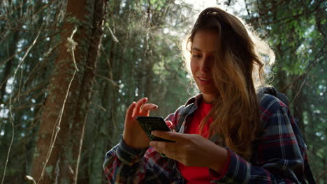 Woman-using-smartphone-in-summer-forest.-Smiling-hiker-scrolling-mobile-phone